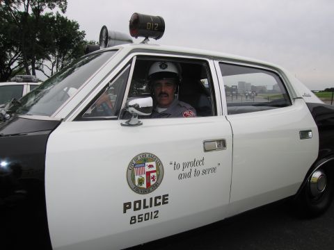 1991 Ford LTD Crown Victoria - man in a white helmet sits inside a white LAPD police car door marked POLICE 85012 with a roof loudspeaker labeled 012.
