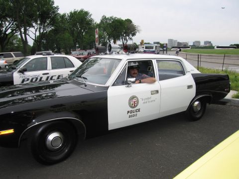 1991 Ford LTD Crown Victoria - black-and-white AMC LAPD police sedan with roof loudspeakers and a driver inside, parked beside a freeway.