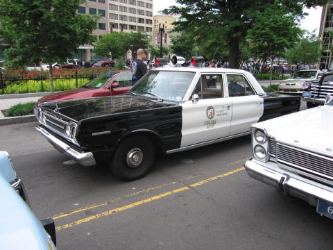1991 Ford LTD Crown Victoria - black-and-white Plymouth LAPD police sedan with a roof loudspeaker parked among other classic cars on a city street.