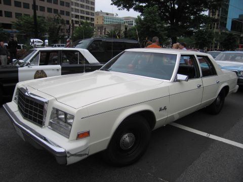 1991 Ford LTD Crown Victoria - late-1970s white Chrysler Newport four-door sedan is parked on city pavement among other classic cars and onlookers.