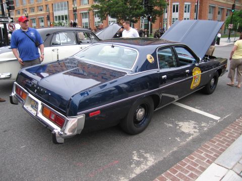 1991 Ford LTD Crown Victoria - dark blue mid-1970s state police four-door sedan with hood and trunk open and a gold door shield is displayed on a city street.