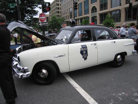 1991 Ford LTD Crown Victoria - two-tone black-and-white early-1950s Ford sedan marked STATE POLICE with an Illinois door emblem sits with its hood open on a city street.