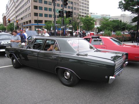 1991 Ford LTD Crown Victoria - dark green mid-1960s four-door sedan with steel wheels sits on a downtown street among spectators and other classic cars.
