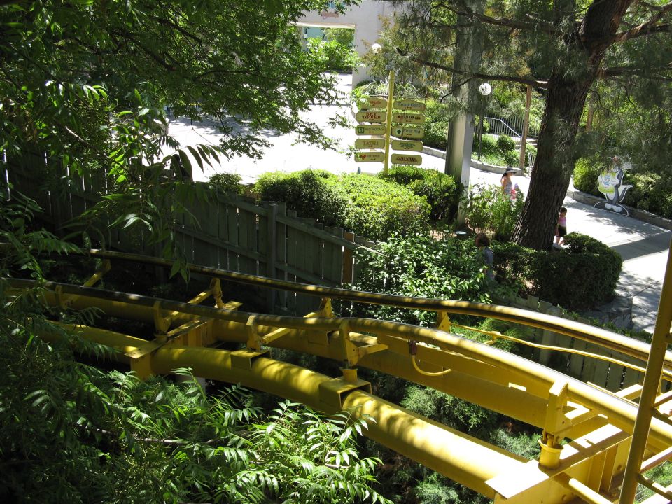 Yellow roller coaster track through trees and foliage with a signpost.
