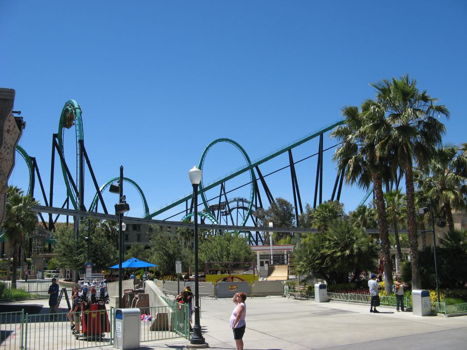 Roller coaster with teal tracks and palm trees under a clear blue sky.