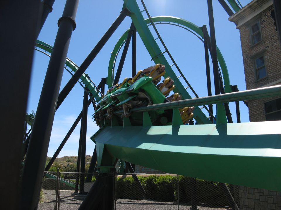 Green roller coaster train with riders in loop beside brick building