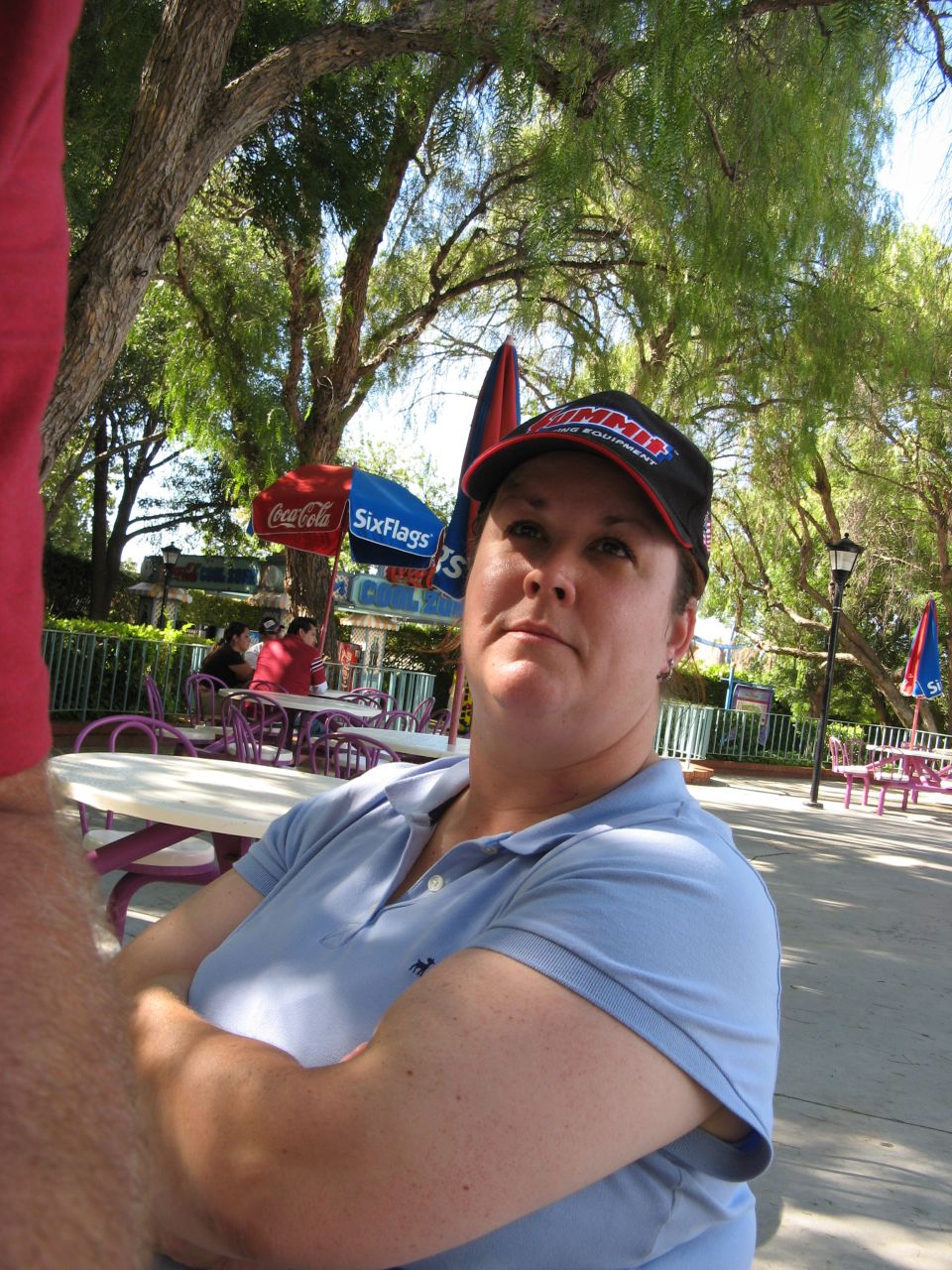 Woman wearing a blue polo shirt and a black baseball cap sitting outdoors.