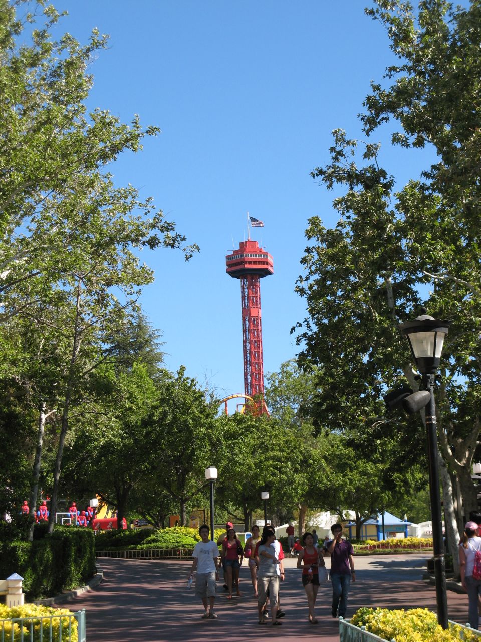 Red observation tower at an amusement park with people walking on a path.