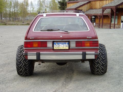 2000 Ford E350 - The rear view of a modified red AMC Eagle wagon with oversized off-road tires. The vehicle has an Alaska license plate that reads "DSB 214".