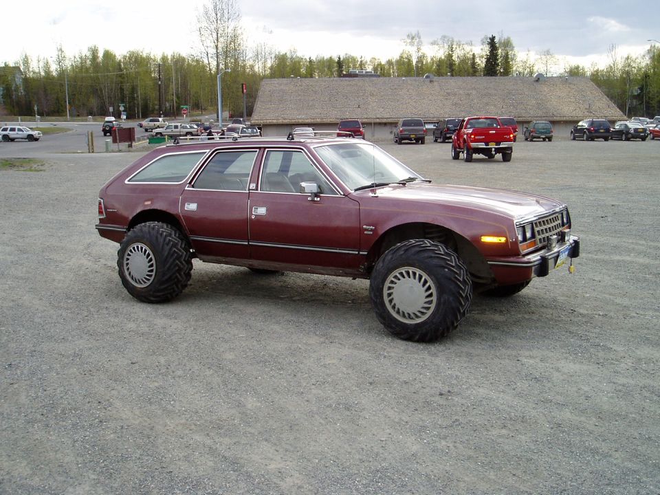 Maroon AMC Eagle wagon with massive off-road tires parked on gravel.