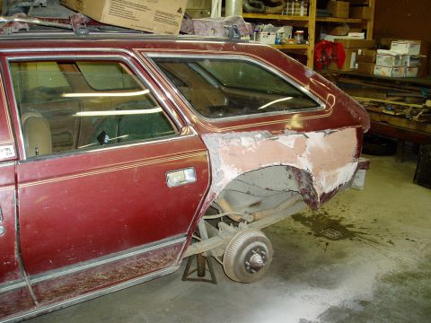 2000 Ford E350 - The rear quarter panel of a dark red station wagon is shown with body filler applied, suggesting ongoing bodywork. The rear wheel is remove…