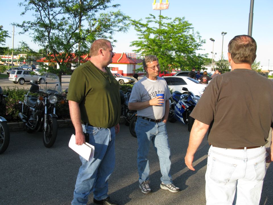 Three men talking in a parking lot near parked motorcycles