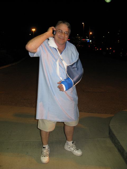 1985 Ford LTD Crown Victoria - Man with an injured arm and in a hospital gown uses a cell phone outdoors at night.