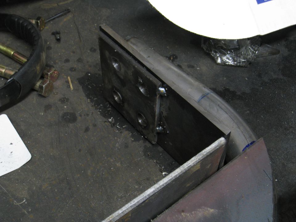 Metal bracket with four bolt holes, attached to a curved metal tube