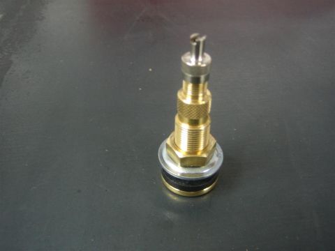 1987 Suzuki Samurai - A single brass tire valve stem is shown against a dark, reflective surface.