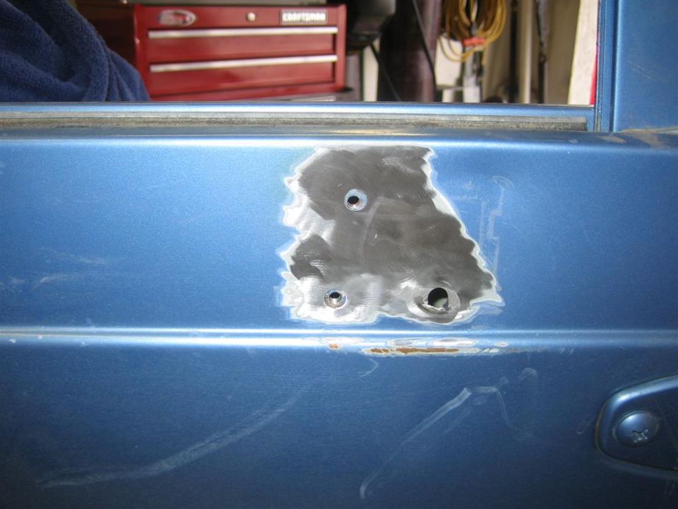 Blue vehicle body panel with sanded area and holes, showing rust.