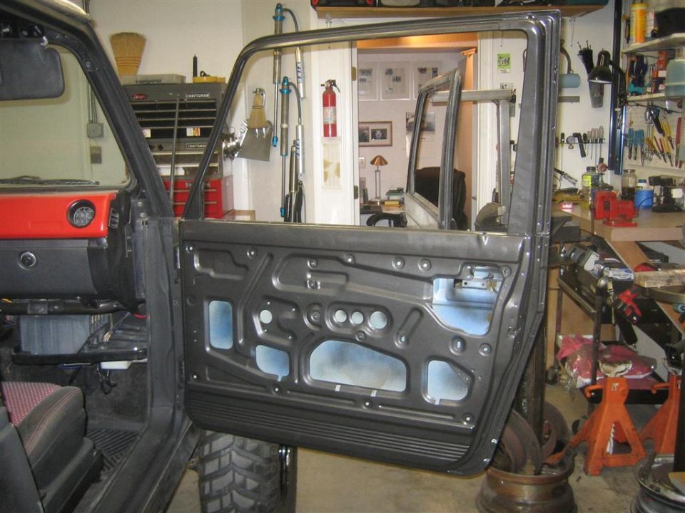 Suzuki Samurai interior with driver's door removed, showing door panel components and garage background.