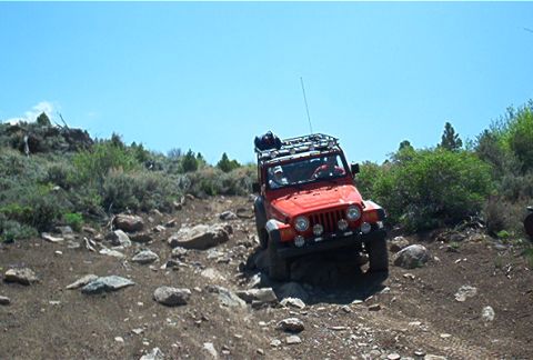 1986 Ford Bronco - A red Jeep Wrangler navigates a challenging, rocky off-road path on a sunny day.