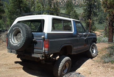 1986 Ford Bronco - 1986 Ford Bronco navigating an off-road trail with trees and hills in the background.