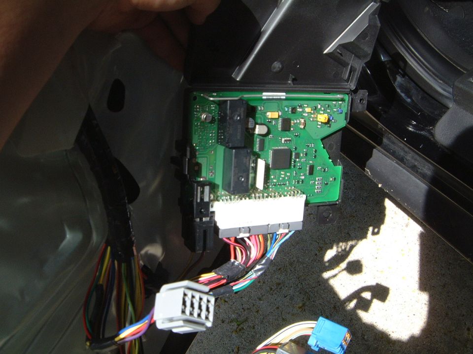 Exposed circuit board of a control module with gray connector and wiring harness inside a car's interior panel area