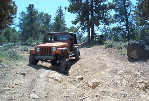 1986 Ford Bronco - A Jeep navigates a rocky, off-road trail under a clear blue sky.