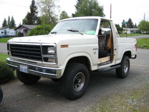 1980 Ford Bronco - 1980 Ford Bronco with driver door ajar, parked outdoors on a paved surface.