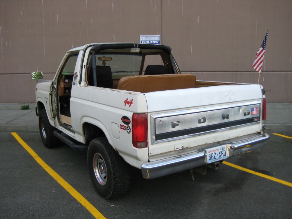 White pickup truck, rear quarter view, driver door open, cargo bed has boxes