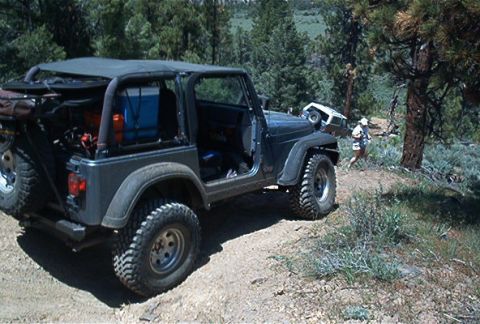 1986 Ford Bronco - Jeep CJ-7 navigating an off-road trail with another Jeep in the distance.