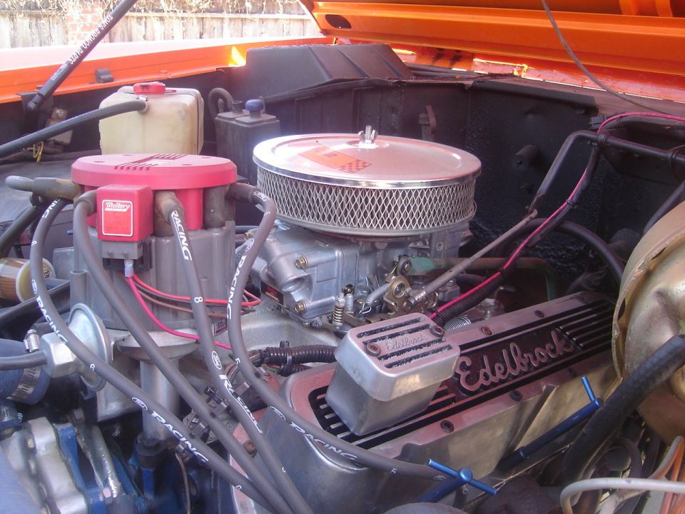 Orange vehicle engine bay with Edelbrock valve covers and a Holley carburetor