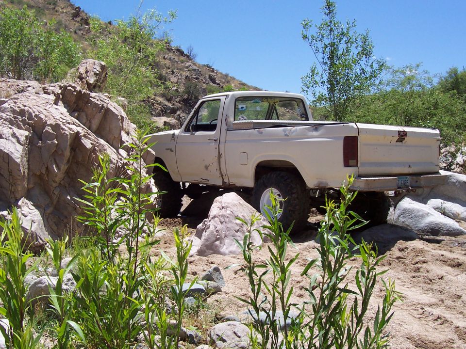 1980 Ford F-150 pickup truck driving over rocks in a dry, desert-like environment