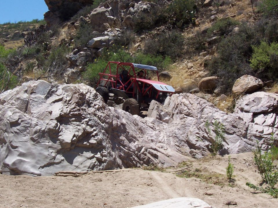 Red off-road buggy with roll cage navigating rocky terrain