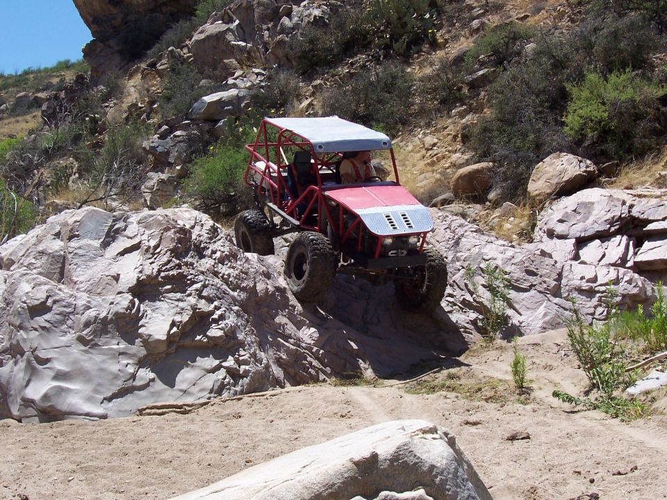 Red off-road buggy with a white canopy navigating a rocky, desert-like terrain