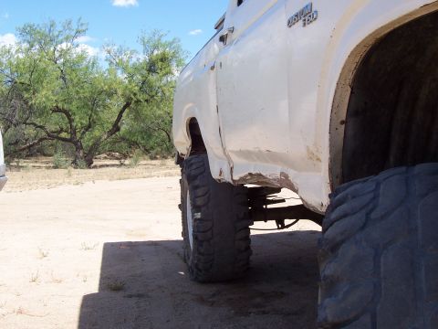 1981 Ford F-150 - This white 1981 Ford F-150 shows significant rust on its lower rear quarter panel and features large off-road tires.