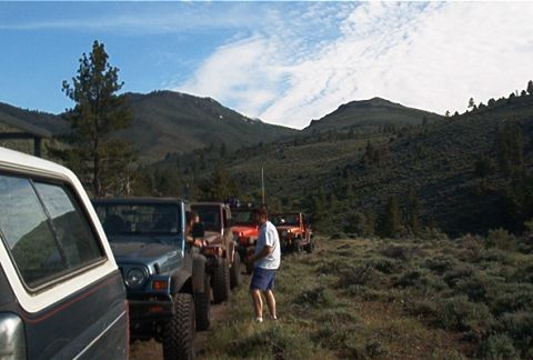 1986 Ford Bronco - Several Jeeps are parked in a line on a mountain trail, with a person walking between them.