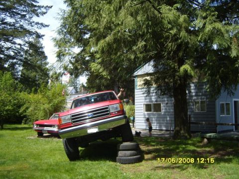 1989 Ford Bronco - A red Ford pickup truck is positioned with its front wheels on stacked tires, demonstrating articulation in a grassy yard.