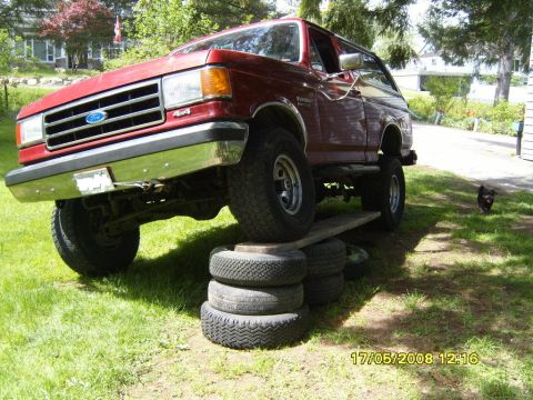 1989 Ford Bronco - A red Ford Bronco is elevated on stacked tires and a wooden plank, showing its articulation.