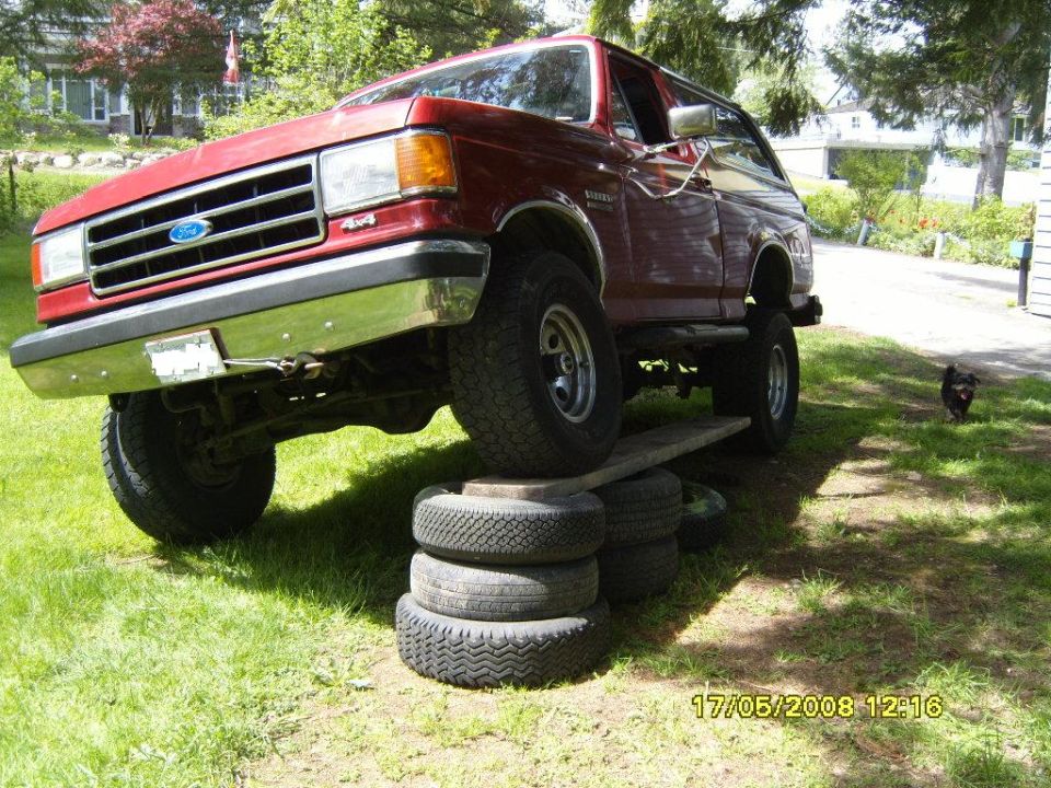 Red Ford Bronco on tires and wood, front passenger side elevated