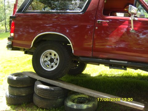 1989 Ford Bronco - Rear quarter view of a red 1989 Ford Bronco, elevated on a ramp constructed from stacked tires.
