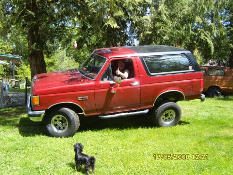 1989 Ford Bronco - A red Ford Bronco with a black top is parked on a grassy lawn, with a person inside giving a thumbs up.