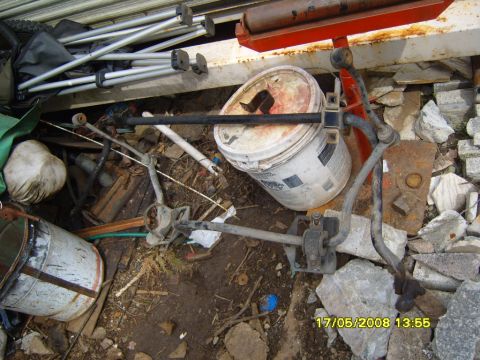 1989 Ford Bronco - A collection of suspension parts, including a sway bar, are scattered among debris and buckets.