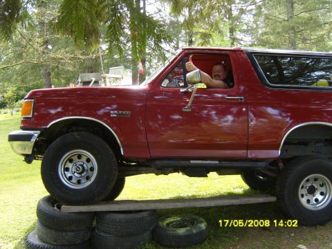 1989 Ford Bronco - A man in a red Ford Bronco gives a thumbs up while the vehicle is positioned on stacked tires and wooden planks.