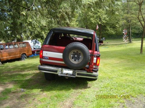 1989 Ford Bronco - Rear view of a red 1989 Ford Bronco, equipped with a spare tire and a Hi-Lift jack, parked outdoors.
