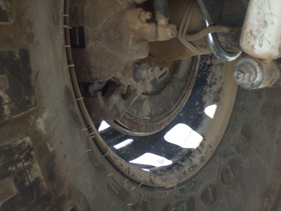 Close-up of a dirty vehicle wheel and brake assembly, showing the tire, rim, and suspension components