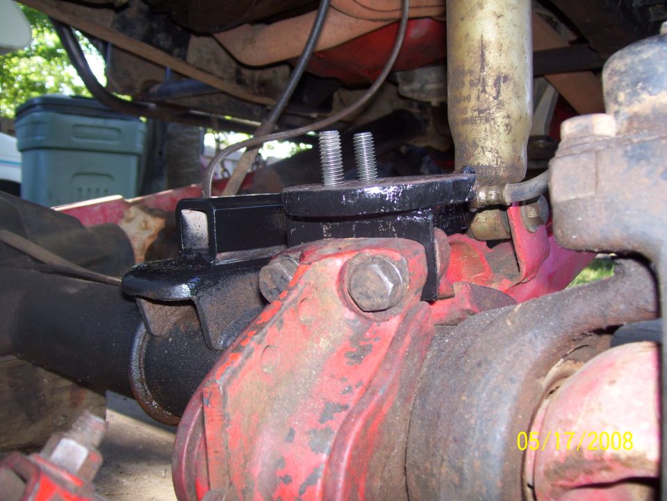 Black metal bracket bolted to red differential housing with two bolts and nuts