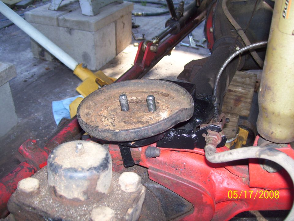 Close-up of a rusty metal part with two bolts, attached to red vehicle components