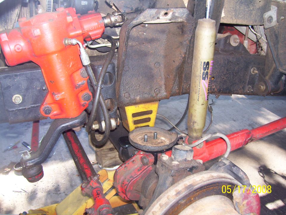 close-up of vehicle's front steering and suspension parts, including a red steering box and a shock absorber