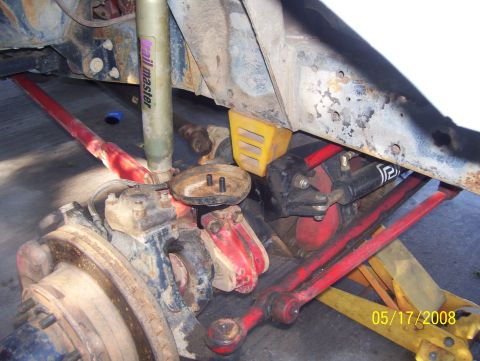 1978 Ford Bronco - Close-up view of vehicle suspension components, including red control arms and a shock absorber.