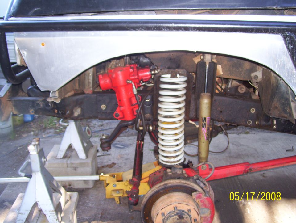 Close-up of red steering gear, white coil spring, and yellow jack under vehicle frame