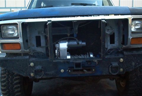 1986 Ford Bronco - The front grille of a truck has been removed to reveal a winch mechanism mounted behind the bumper.