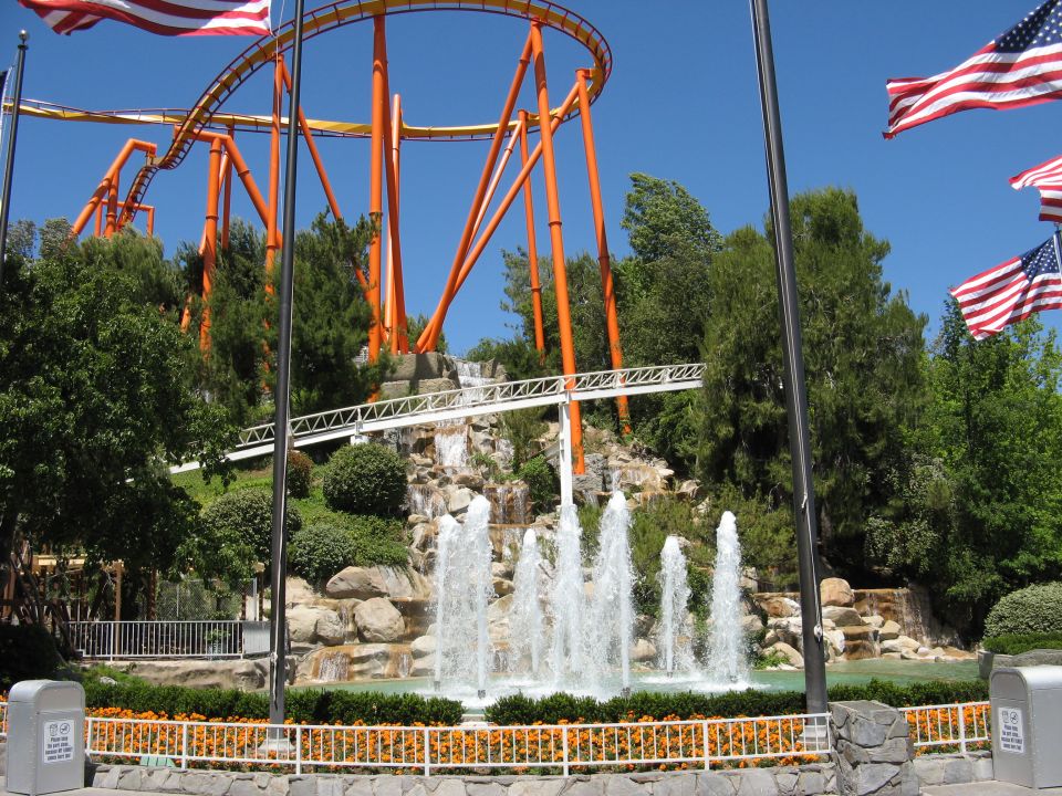 Roller coaster with orange supports above a fountain and landscaping